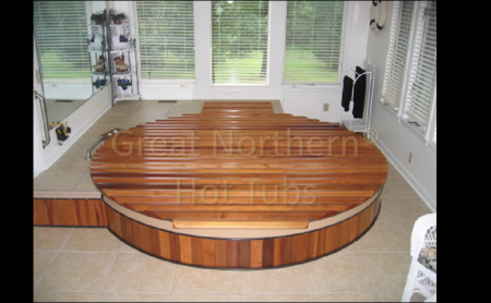 <p>Large round hot tub sunken into the floor of a therapy room. Photo also shows the wood, roll-up cover.</p>