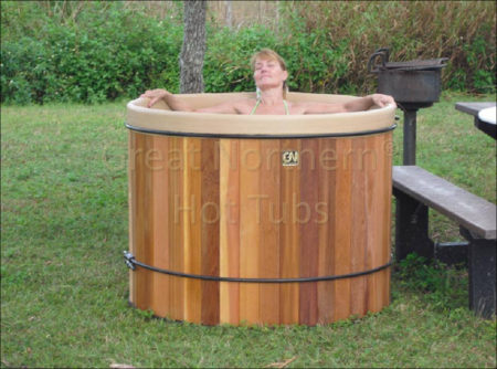 <p>Woman sitting in a portable Great Northern cedar hot tub at a campground.</p>