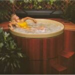 Blonde woman in yellow swimsuit relaxing in a round redwood hot tub