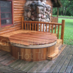 Outdoor redwood hot tub with a rollup cover, situated near a log cabin for a rustic and relaxing retreat