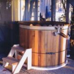 Cedar hot tub with a custom-fit wooden rollup cover placed outside a cozy home